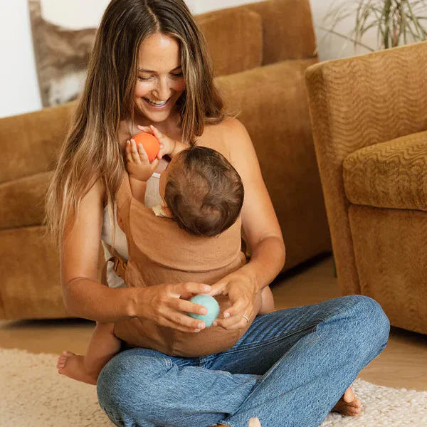Mom sitting on floor with Baby in a baby carrier playing with toys