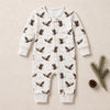 A baby long-sleeve footless one-piece romper with an allover eagle print, laid flat on a beige background with pine branches and a pinecone.