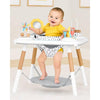 Baby sitting in an activity table with toys around, smiling.